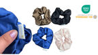 Set of satin scrunchies in blue, brown, black, and pink with a hand holding a blue scrunchie.
